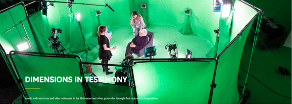 Bilete av eit rundt/ovalt rom sett ovanfrå, sett saman av grøne tekstilskjermar. I midten av rommet sit ei eldre, kvit kvinne i svarte klede. To yngre, kvite kvinner står rundt ho og snakkar til henne, den eine kvinna held på ei blokk i handa. Mange kameraer og elektronisk utstyr er plassert rundt veggen i rommet, og peikar mot midten av rommet. Teksten Dimensions in testimony står med kvit skrift over. 